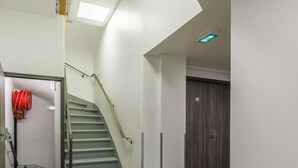 Un intérieur propre et moderne, avec un escalier, une lance d’incendie rouge et une porte en bois.