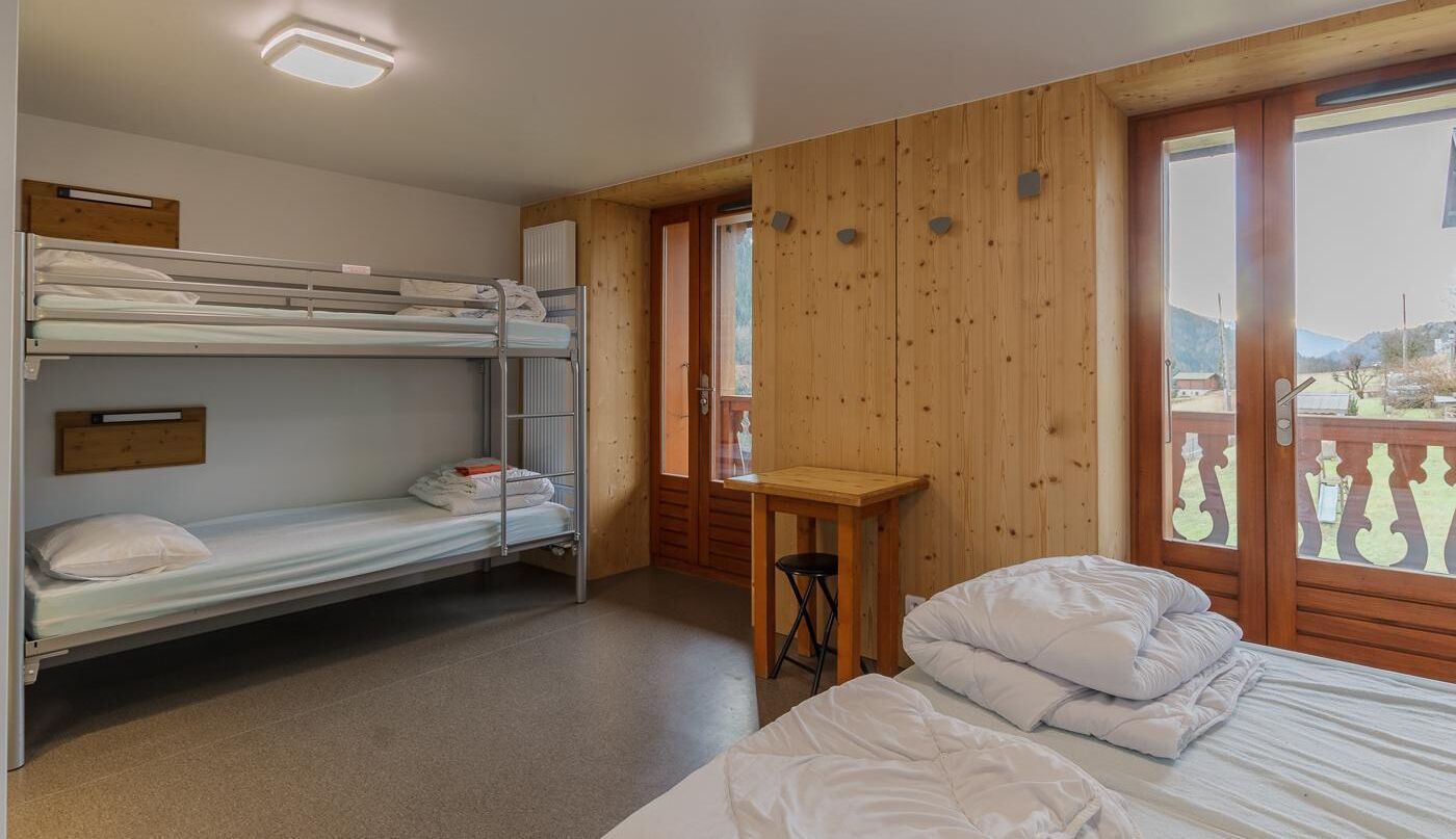 A room with bunk beds, a wooden table, and a window with a view of the outdoors.