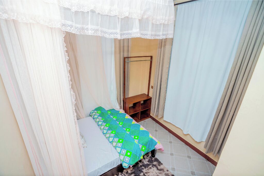A small, neatly arranged bedroom with a single bed, a wooden nightstand, and a mirror on the wall.
