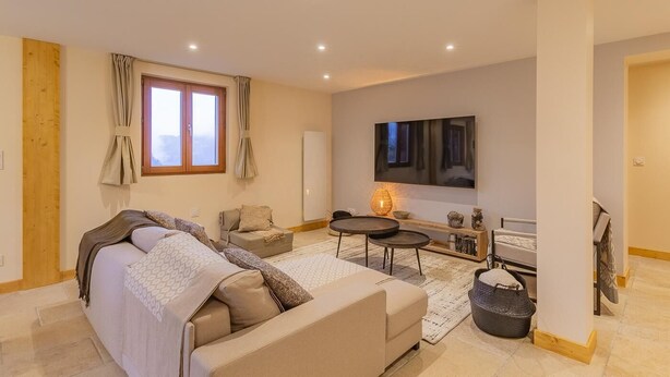 A modern bedroom with a large bed, a sofa, a TV, and a small table with a lamp.