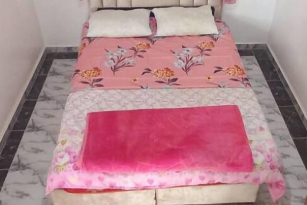 Quarto com cama, cortinas rosa, cabeceira e colcha floral.