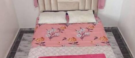 Een slaapkamer met een bed, roze gordijnen, een hoofdeinde en een bloemenbedekking.