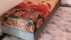 A single bed with a patterned bedspread, a grey upholstered headboard, and a red curtain. - Tranquil Rooms in Agadir (Agadir)