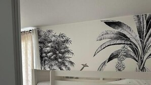 Ein Stockbett mit Wandgemälde im tropischen Stil, eine weiße Tür und ein gemustertes Teppich.