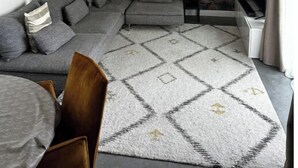 Ein modernes Wohnzimmer mit einem grauen Ecksofa, einem gemusterten Teppich und einer Deckenleuchte.