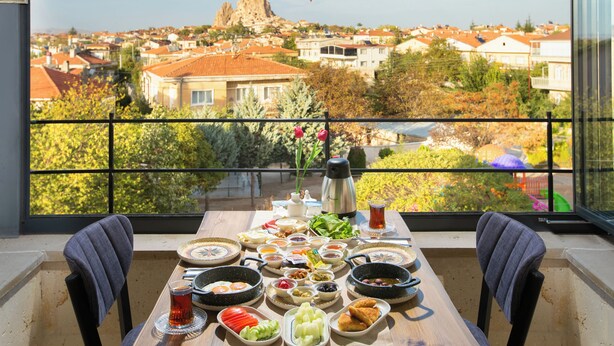 A balcony table with a view of a town and a mountain, set with breakfast items and a thermos. - Cappadocia Fiesta Stone House (Nevsehir)