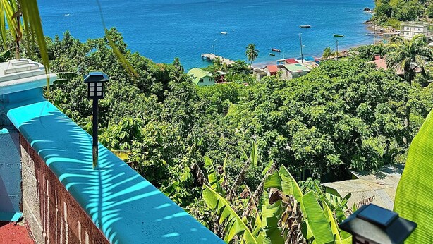 A coastal view with a clear sky, a blue railing, and lush greenery. - The Big Blue Condo (Soufriere)