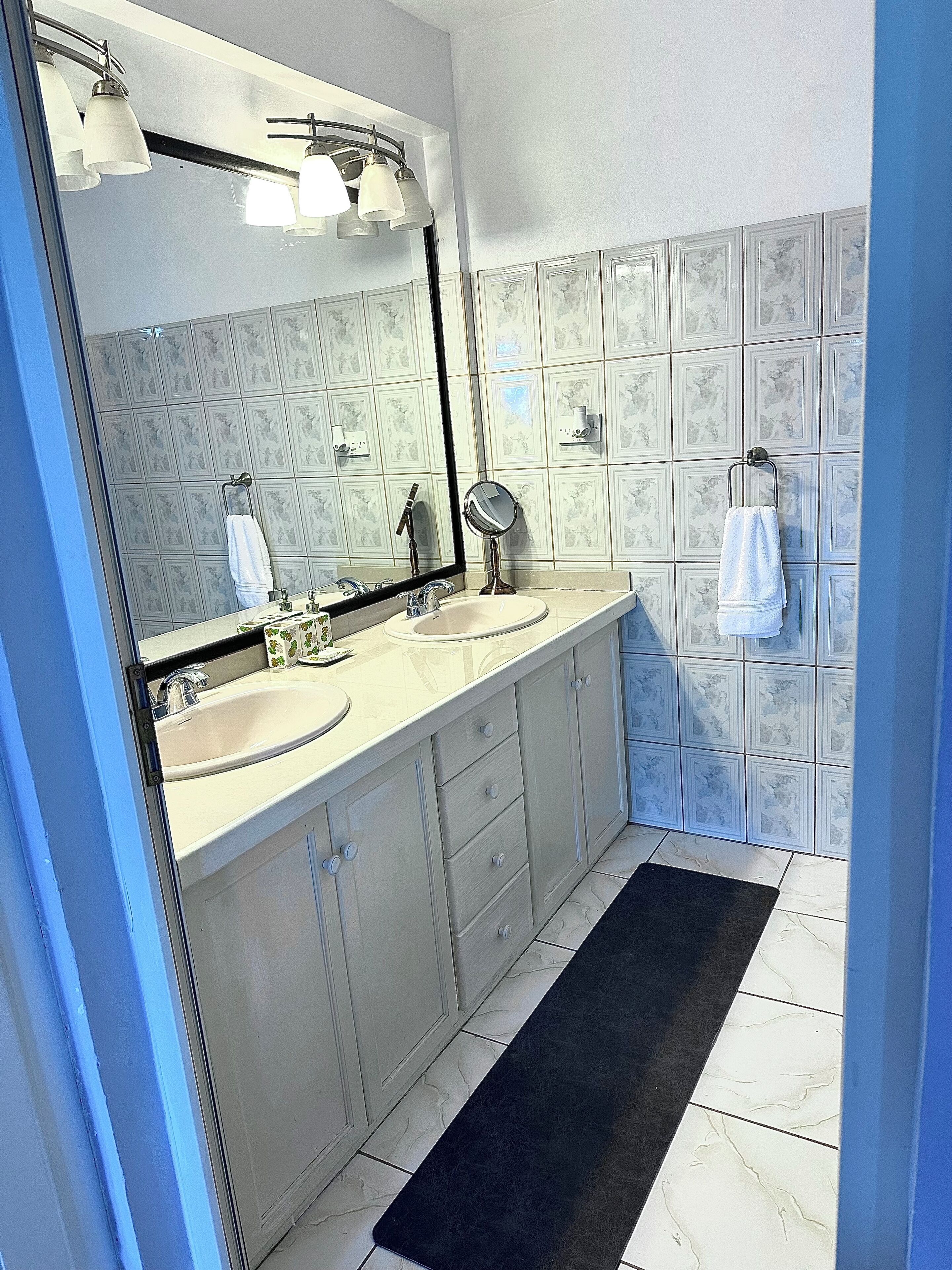 Une salle de bain avec deux lavabos, un grand miroir et des murs carrelés.