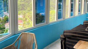 A room with large windows, a tiled floor, a round table, wicker chairs, and a sofa. - The Big Blue Condo (Soufriere)