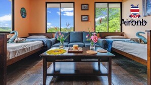 Une pièce confortable avec un canapé, deux lits simples, une table basse agrémentée de fleurs et une vue sur la verdure.