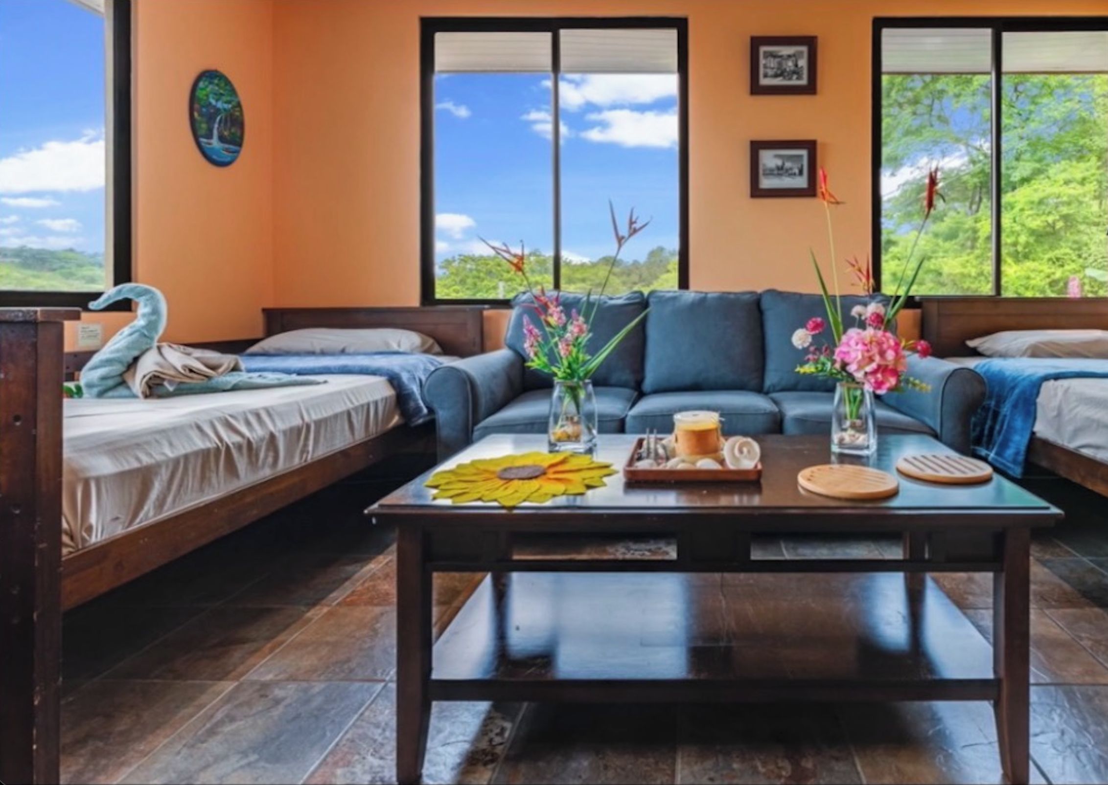 Un cuarto acogedor con un sofá, dos camas individuales, una mesita de centro con flores y vistas a zonas verdes.