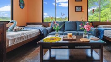 Un cuarto acogedor con un sofá, dos camas individuales, una mesita de centro con flores y vistas a zonas verdes.