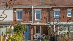 A residential property with a brick facade, a small patio with a table and chairs, and a blue door. - Marrams View | Winterton Cottages (Winterton On Sea)