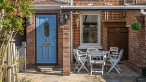 A brick house with a blue door, white outdoor furniture, and a small garden area. - Marrams View | Winterton Cottages (Winterton On Sea)