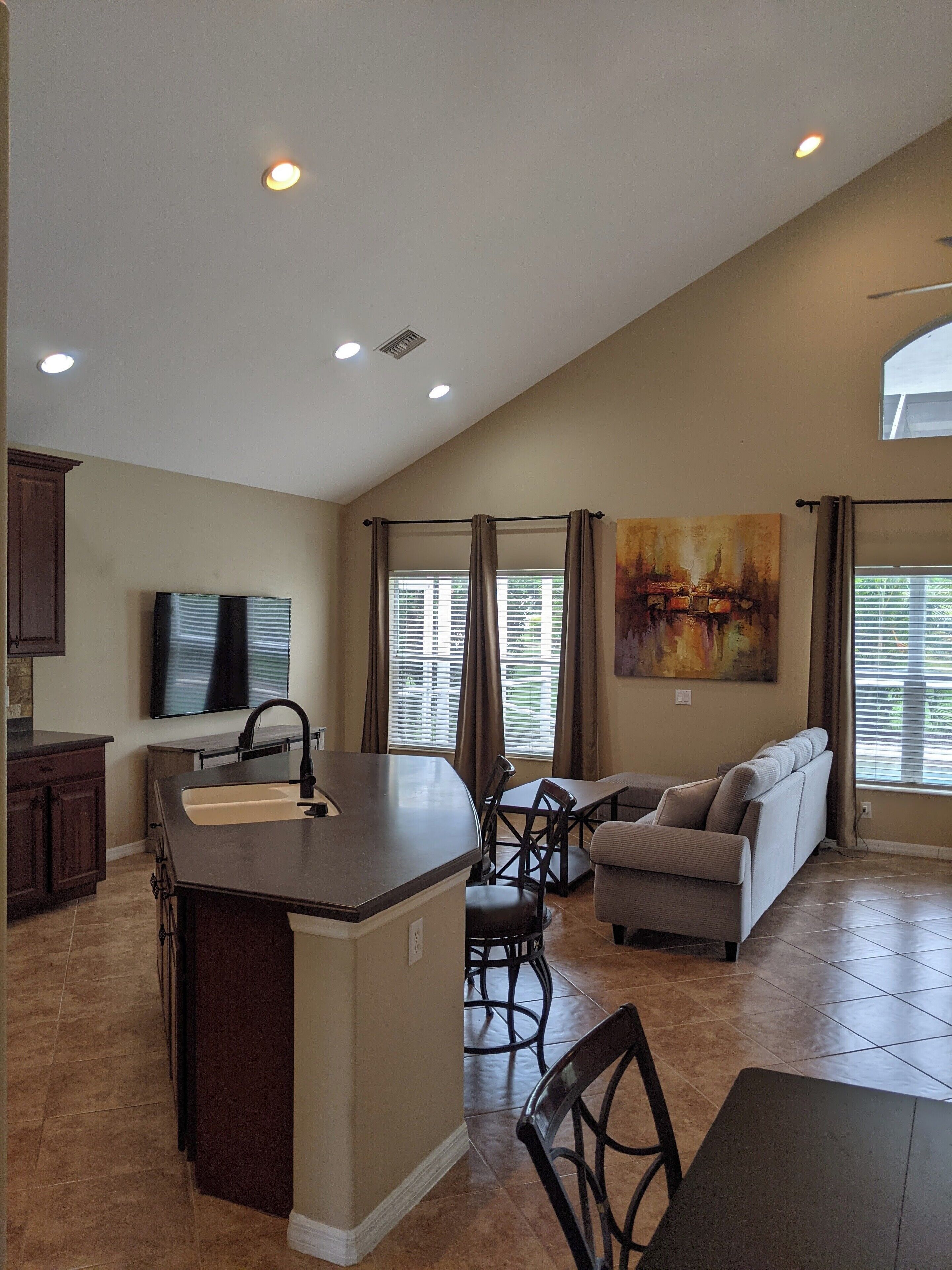 A spacious kitchen with a central island, dining area with a sofa and chairs, and a large window with blinds.