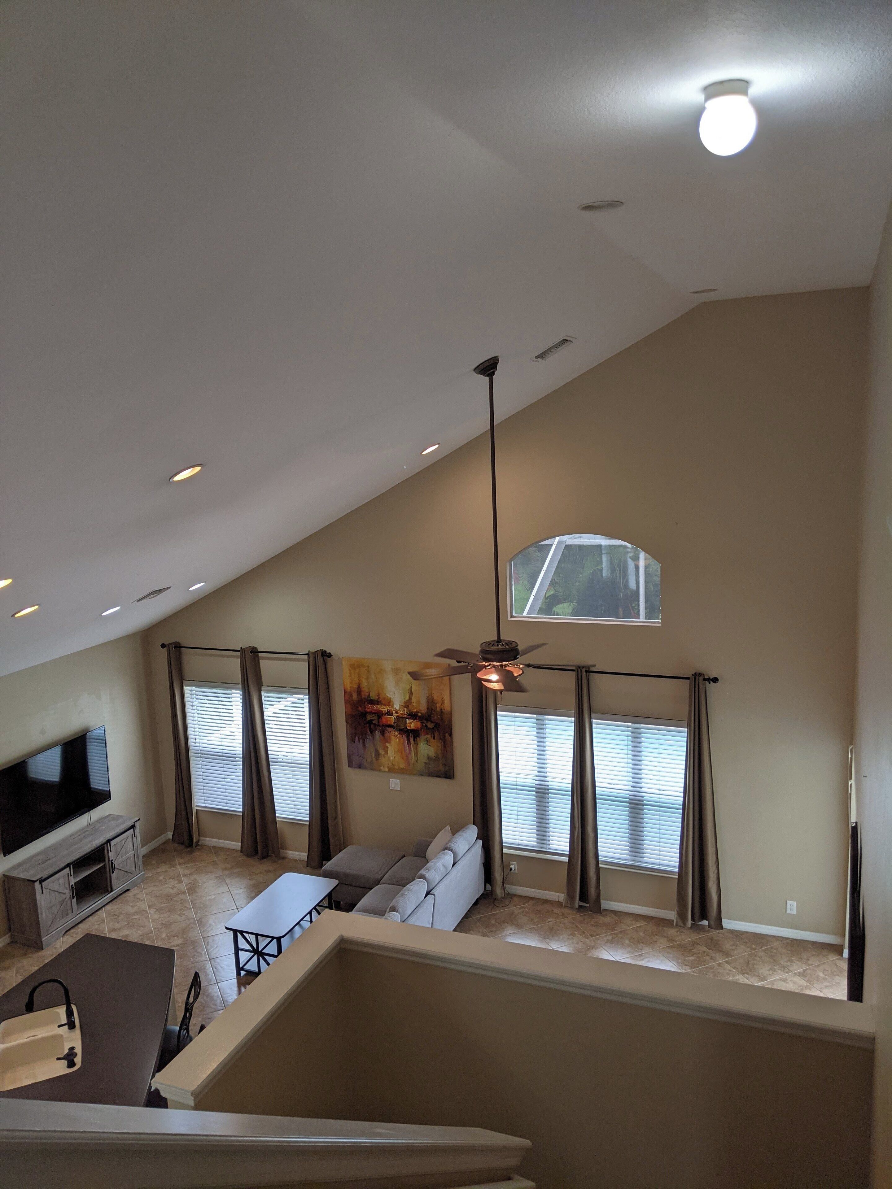 A spacious living area with a high ceiling, a ceiling fan, and a large window with blinds.