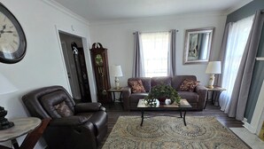 Un salon avec un tapis à motifs, un canapé, une table basse, une horloge et une lampe.