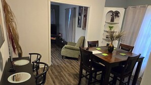 Un coin repas avec une table et des chaises en bois, un petit espace cuisine équipé d’un évier, et un couloir menant à une autre pièce.