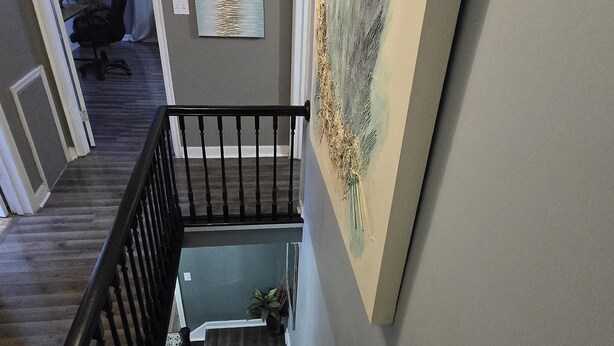 Un escalier avec une rampe noire mène à un palier. Un tableau est accroché au mur, au-dessus de l’escalier.