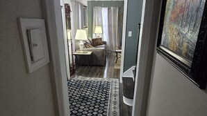Un couloir mène à une chambre à coucher qui contient un lit, une table de chevet, une lampe et un tableau accroché au mur.
