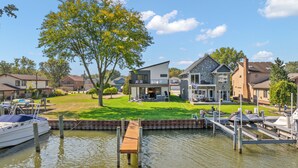 A residential area with modern houses, a dock, and a grassy lawn. - Manse Island: Sizzle by the River – Hot Tub, Fire Pit, and Summer Fun (Harrison Township)