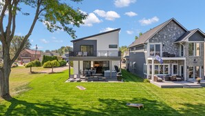 A two-story house with a balcony and a patio area. - Manse Island: Sizzle by the River – Hot Tub, Fire Pit, and Summer Fun (Harrison Township)
