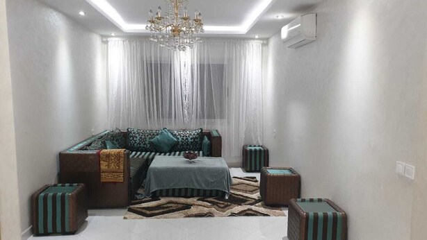 A modern living room with a sofa set, a chandelier, and striped ottomans. - Super City Center Apartment with Parking  (Tanger)