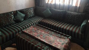 A corner sofa with patterned cushions and a matching ottoman, set against a textured wall with a window providing natural light. - Super City Center Apartment with Parking  (Tanger)