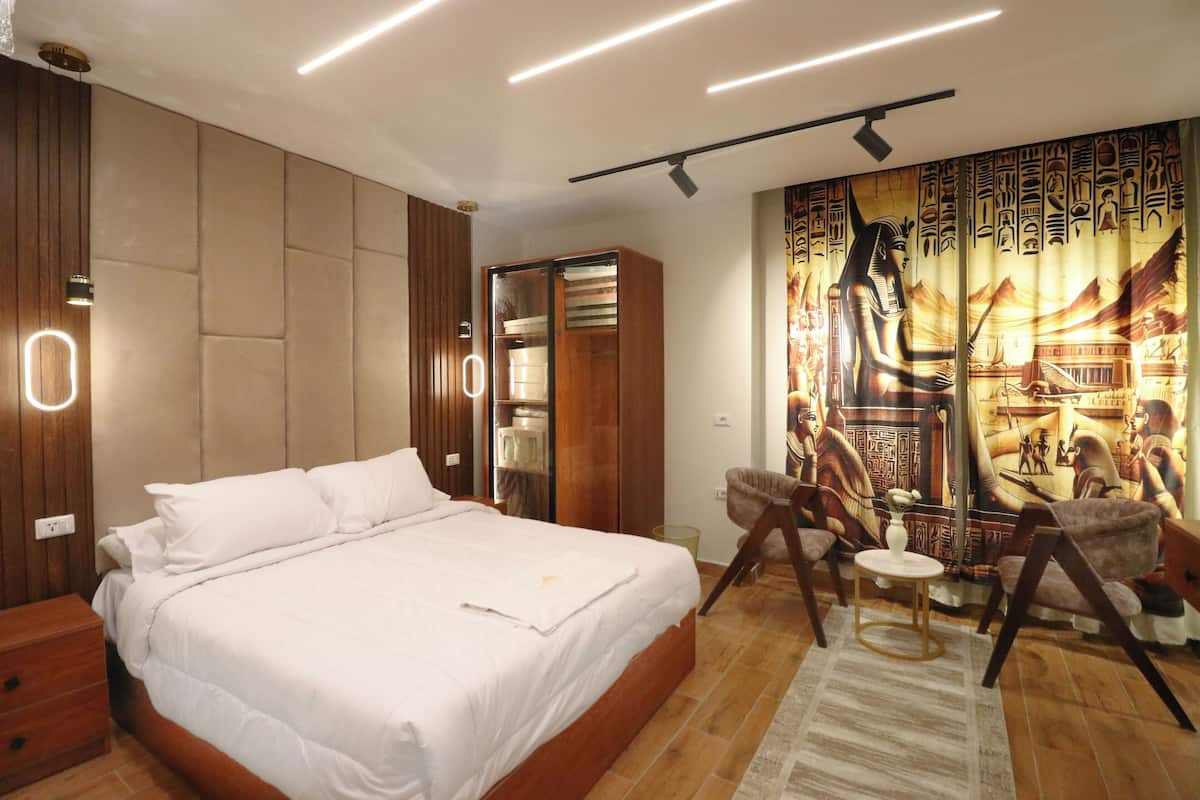 A modern bedroom with a large bed, wooden wardrobe, and a mural of ancient Egyptian figures.