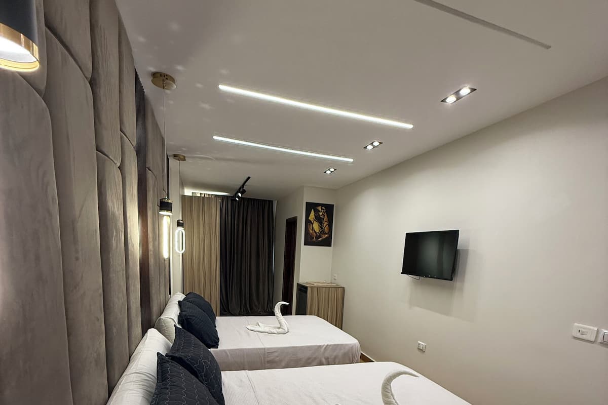A modern hotel room with two beds, a flat-screen TV, and a large window.