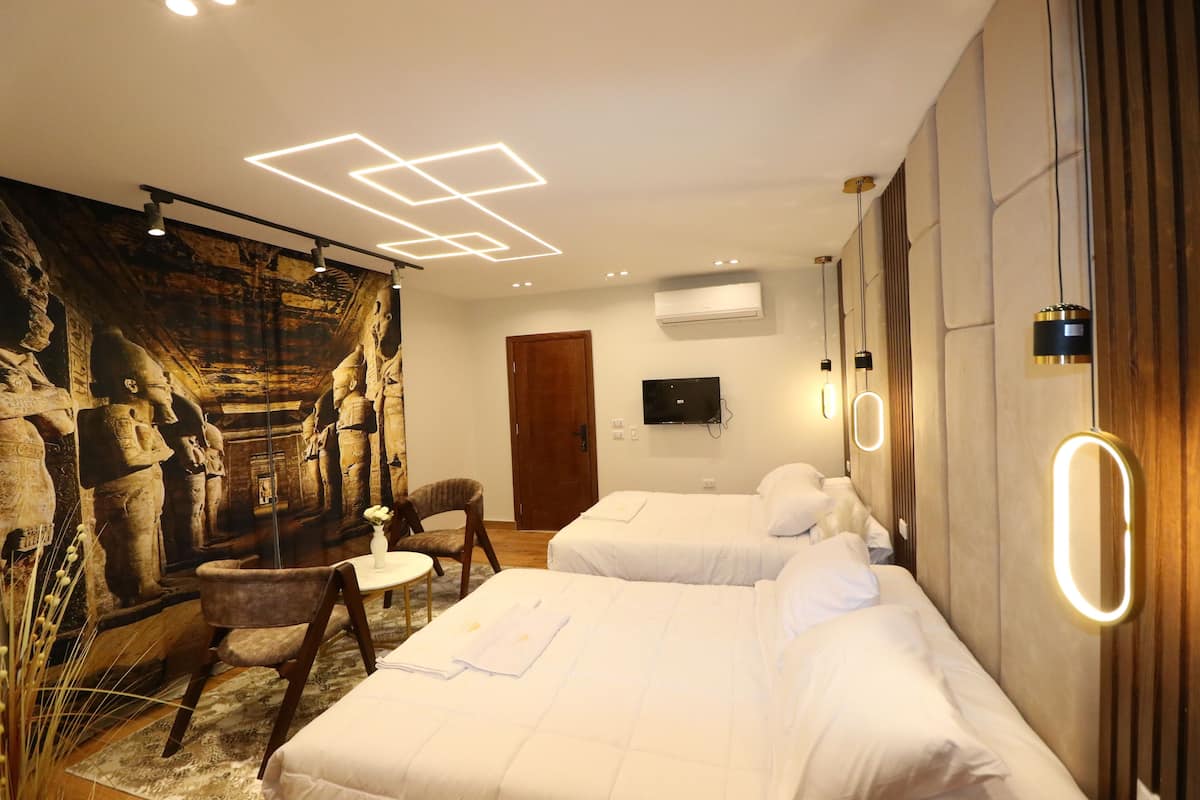 A hotel room with two beds, a small table, a chair, and a mural on the wall.