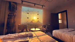 Ett hotellrum med två sängar, ett stort fönster med utsikt över en pyramid och ett litet bord med stolar.
