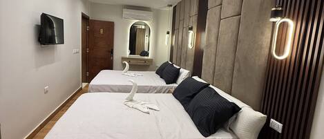 A modern hotel room with two beds, wooden flooring, a flat-screen TV, and a large mirror.