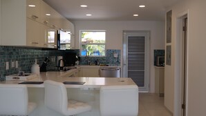 A modern kitchen with white cabinetry, a central island with seating, a window with a view of greenery, and a microwave on the wall.