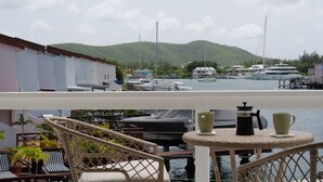 A balcony with wicker furniture, a table with two cups, and a view of a marina with boats and houses in the background.