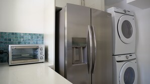 A kitchen with a stainless steel refrigerator, a built-in oven, and a stacked washer and dryer.
