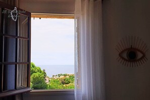 Quarto com janela, decoração em forma de olho na parede e vista para áreas verdes e edifícios.