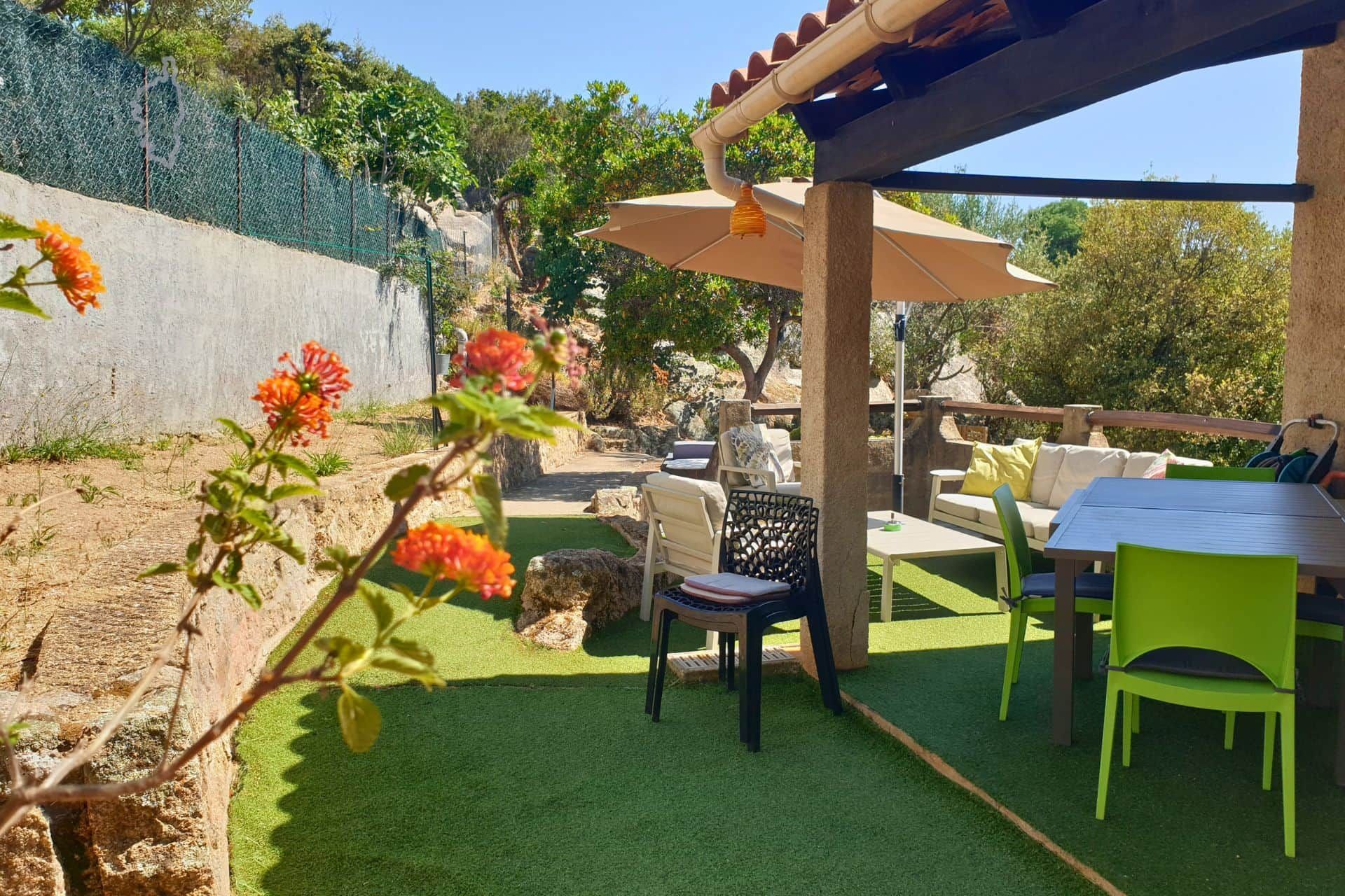 An outdoor patio area with artificial grass, a table, chairs, and a pergola structure.