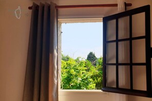 A room with a window, curtains, and a view of greenery outside. - Minavita (Pietrosella)