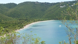 A coastal landscape with a beach, clear blue waters, and green hills in the background. - Luxurious Villa w/ Stunning Ocean Views & Pool (St. Thomas)