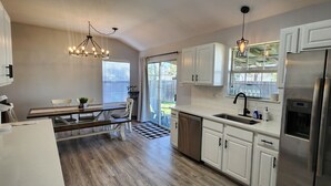 Een moderne keuken met witte kasten, roestvrijstalen apparatuur en een eethoek met een houten tafel en stoelen.