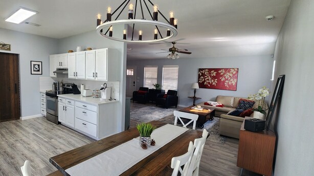 Een moderne keuken met witte kasten, een eethoek met een houten tafel en een woonkamer met een bank en salontafel.