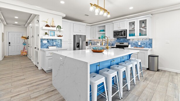 A modern kitchen with white cabinets, a large island with bar stools, a blue tiled backsplash, and a wooden floor. - Upscale New Build with Private Pool, Steps to the Beach (South Padre Island)