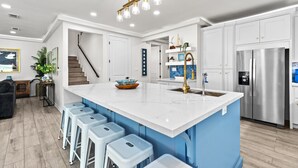 A modern kitchen with a large island, white cabinets, a stainless steel refrigerator, and a blue accent wall. - Upscale New Build with Private Pool, Steps to the Beach (South Padre Island)