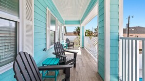 A covered porch with turquoise siding, two Adirondack chairs, and a small table. - Upscale New Build with Private Pool, Steps to the Beach (South Padre Island)