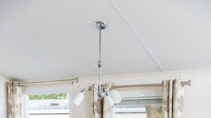 Un comedor con una mesa de madera y sillas blancas, una lámpara de araña y cortinas.