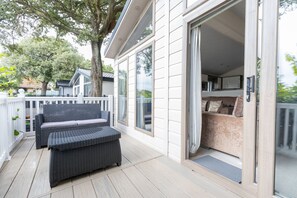 A covered outdoor area with a wicker sofa and a sliding glass door leading to a room with a cushioned bench. - Dun a Ri - a Sandhills lodge providing a coastal sanctuary. (Christchurch)