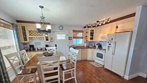 A kitchen with wooden flooring, white cabinets, a dining table with chairs, and a refrigerator.