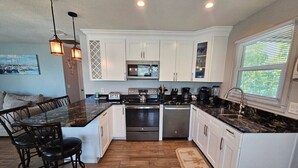 A modern kitchen with white cabinets, a central island, and a dining area with black chairs. - El Palmar Unit 2 Third Level from Beach (Indian Rocks Beach)