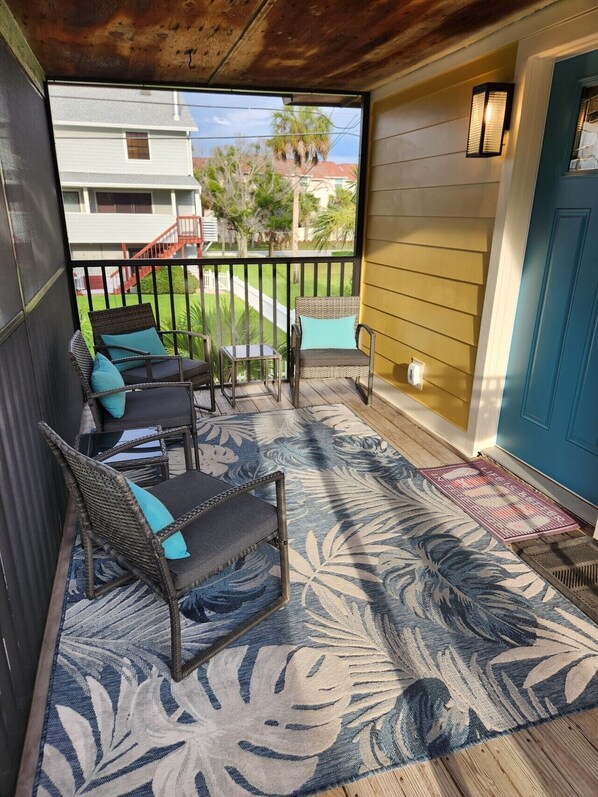 Une véranda aménagée avec des meubles en osier, un tapis à motifs et une vue sur une rue résidentielle.